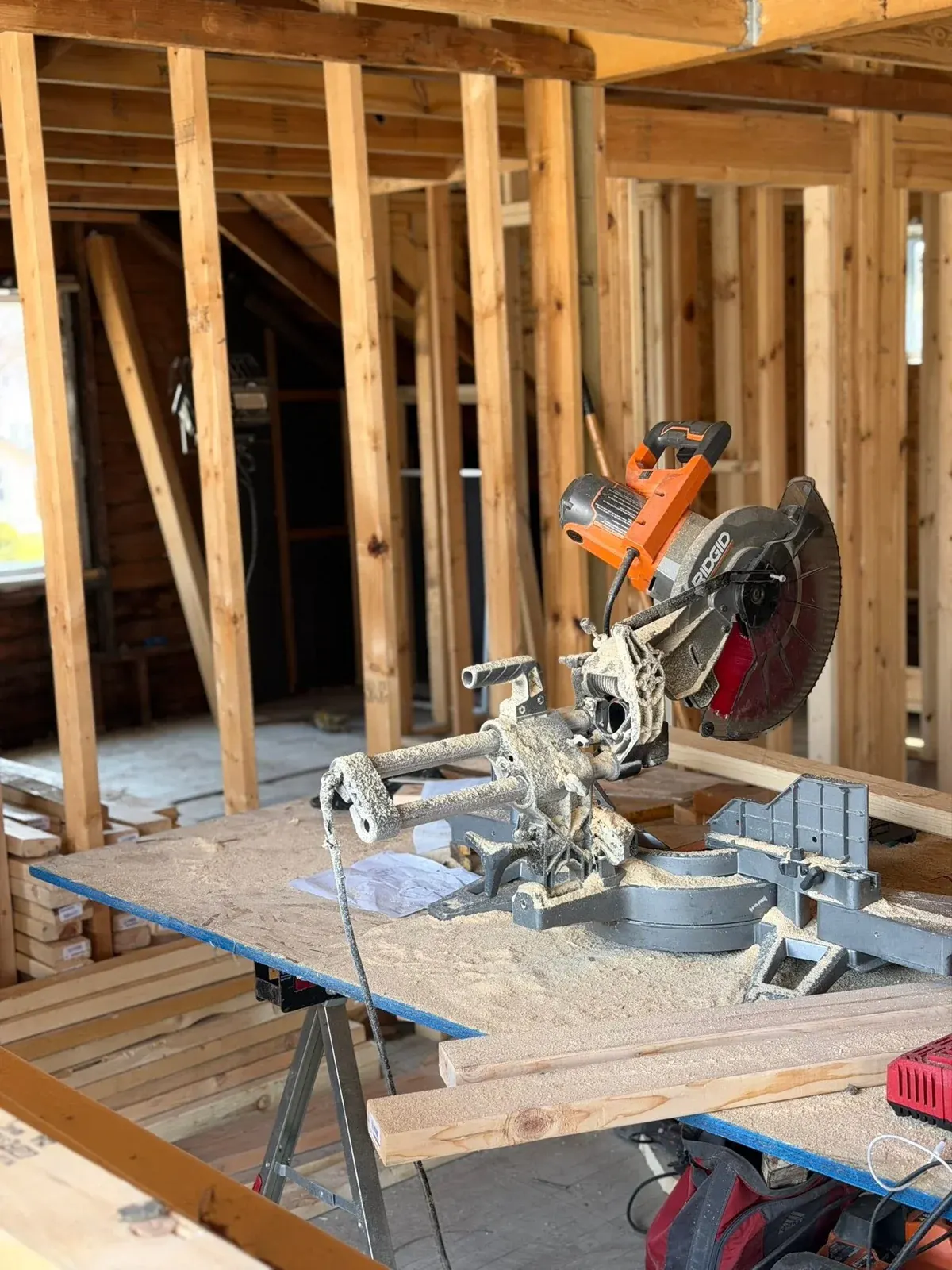 Miter saw covered in sawdust on work table inside residential construction framing