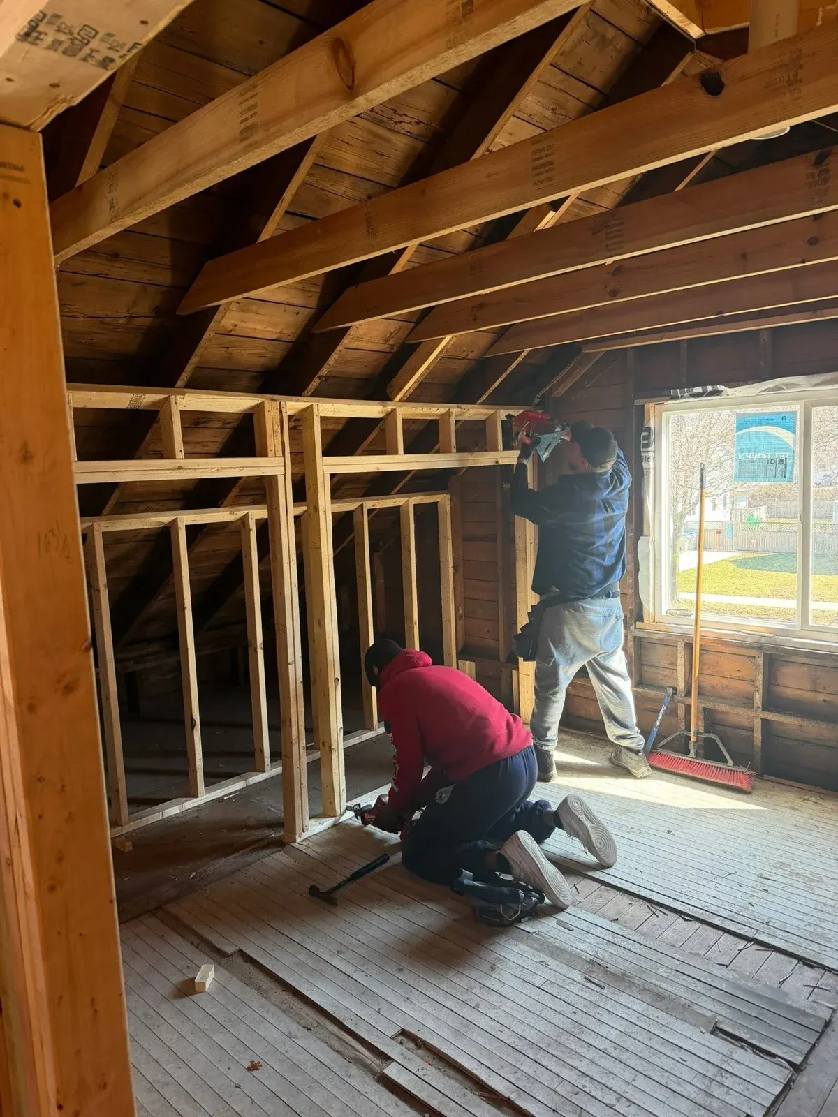 Two workers renovating interior of wooden framed house structure with exposed beams and framing