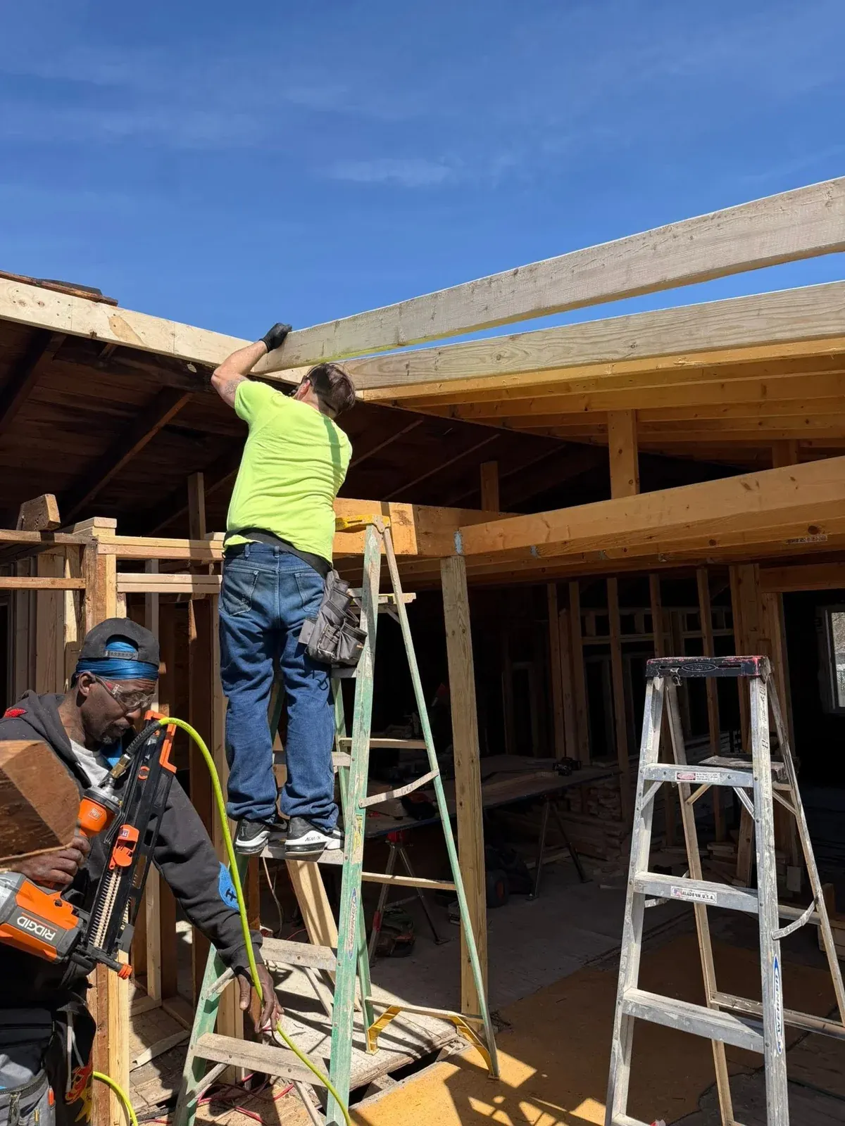 Construction worker in safety gear installing wooden beam on residential framing project