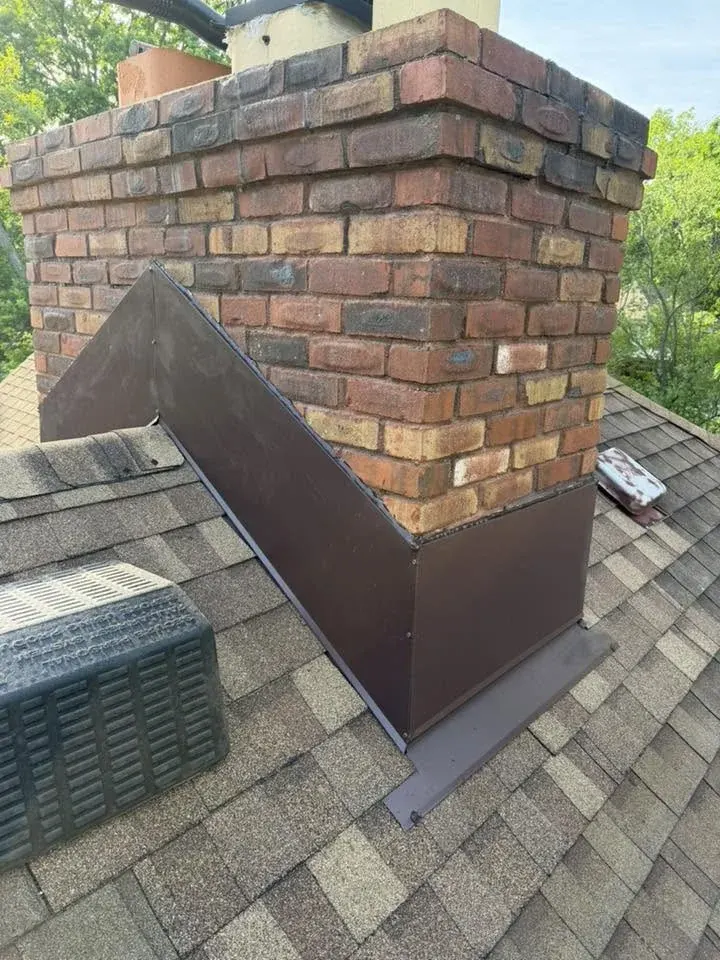 Brick chimney on residential roof with metal flashing and shingles