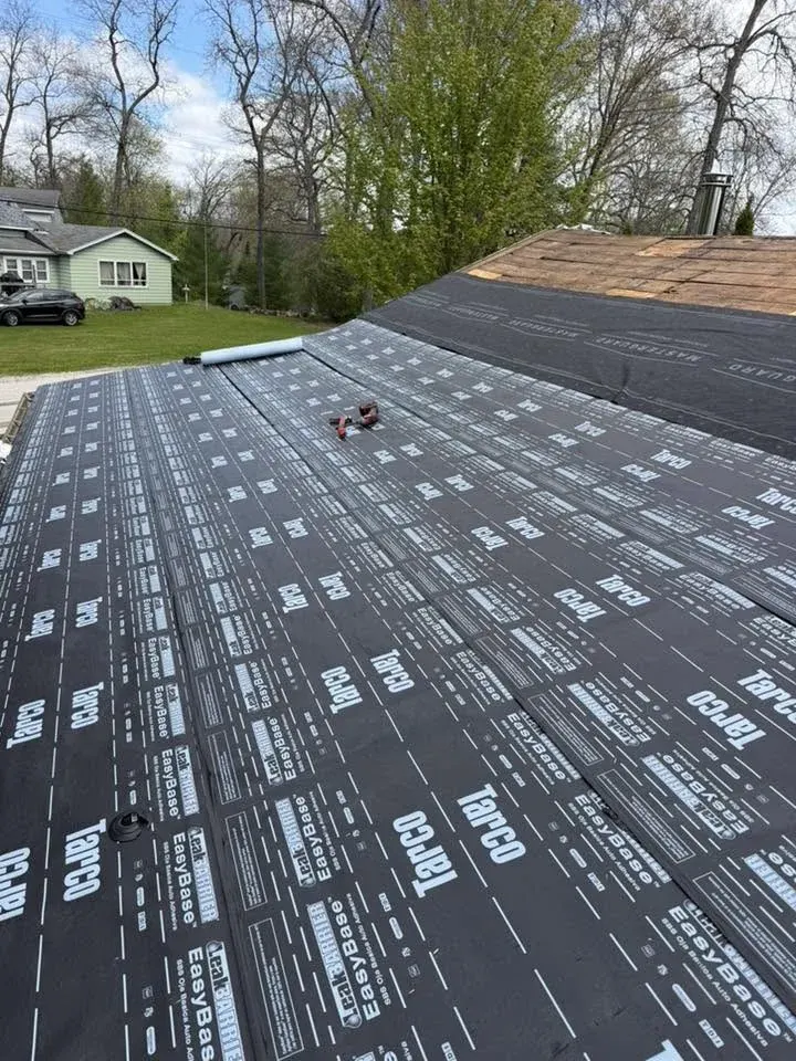 Roof underlayment installation showing black synthetic membrane with white printed text and grid pattern on residential home