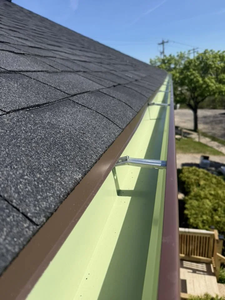Close-up of gray asphalt shingles and light green gutter system on residential roof edge