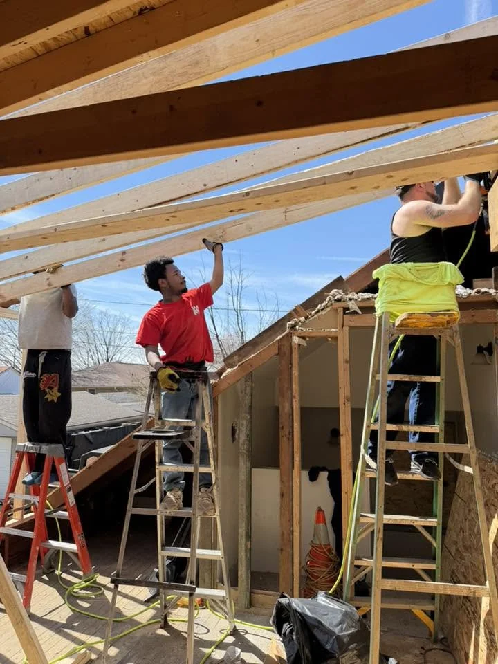Workers installing wooden roof beams on residential construction framing under clear blue sky