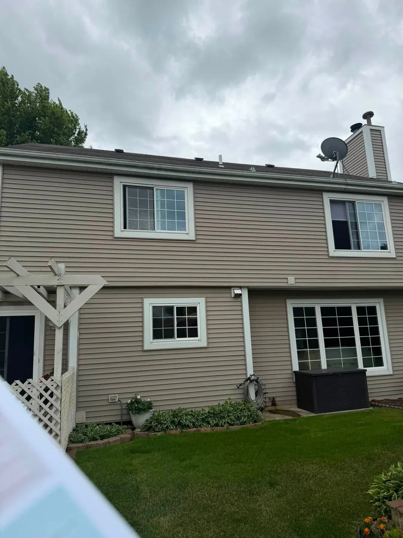 Two-story beige house with white trim windows, covered porch, and satellite dish on roof