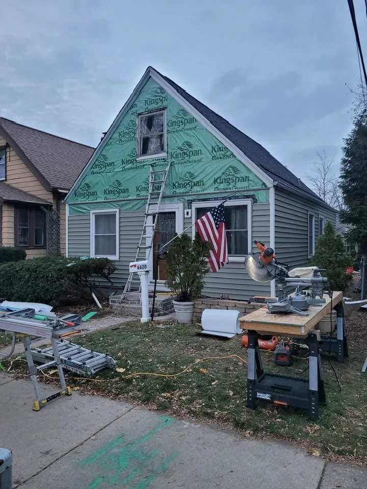 Home under renovation with green Kingspan underlayment, ladder, work table, and tools in yard