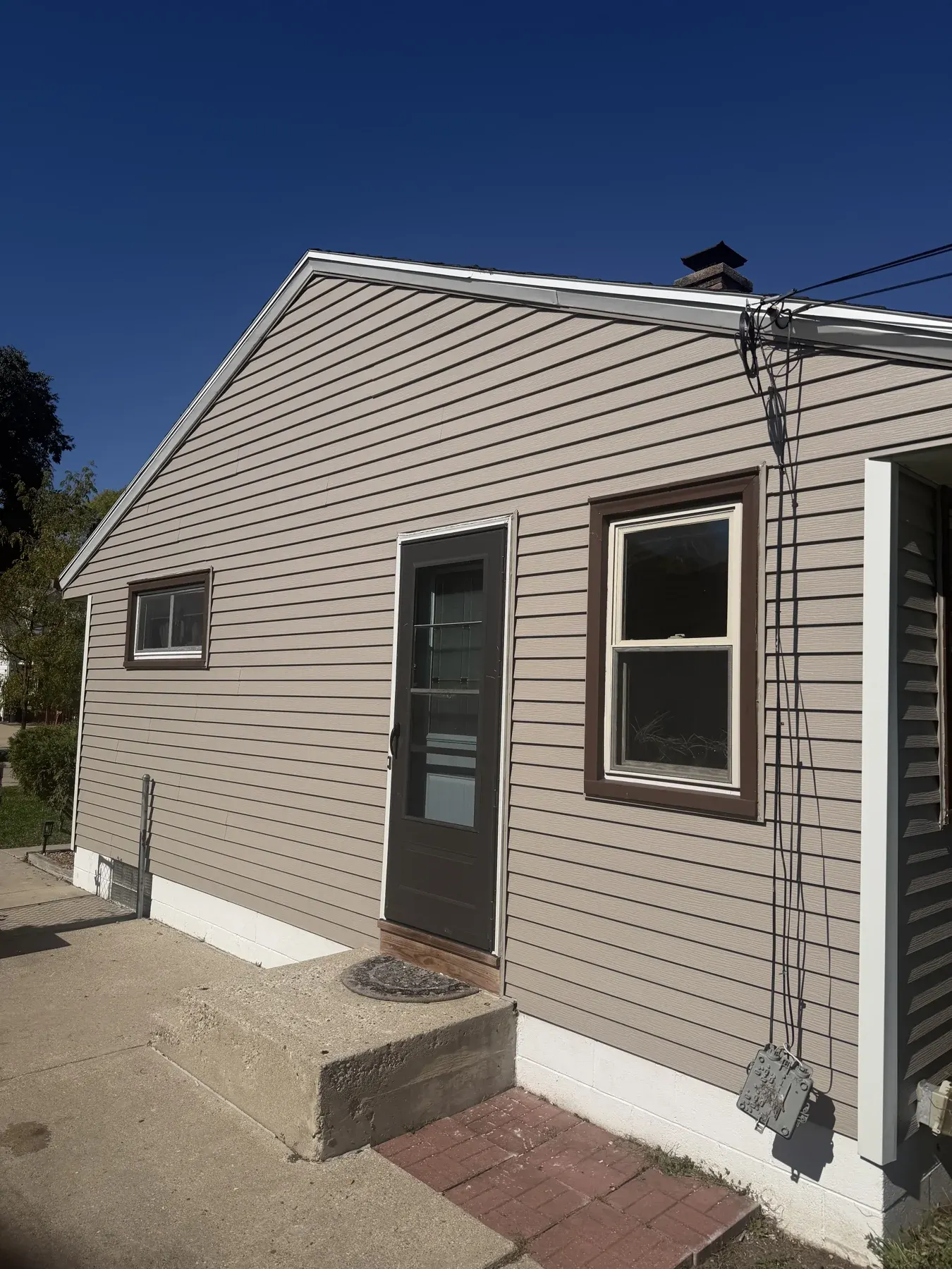 Small residential home with beige vinyl siding and gabled roof on clear day