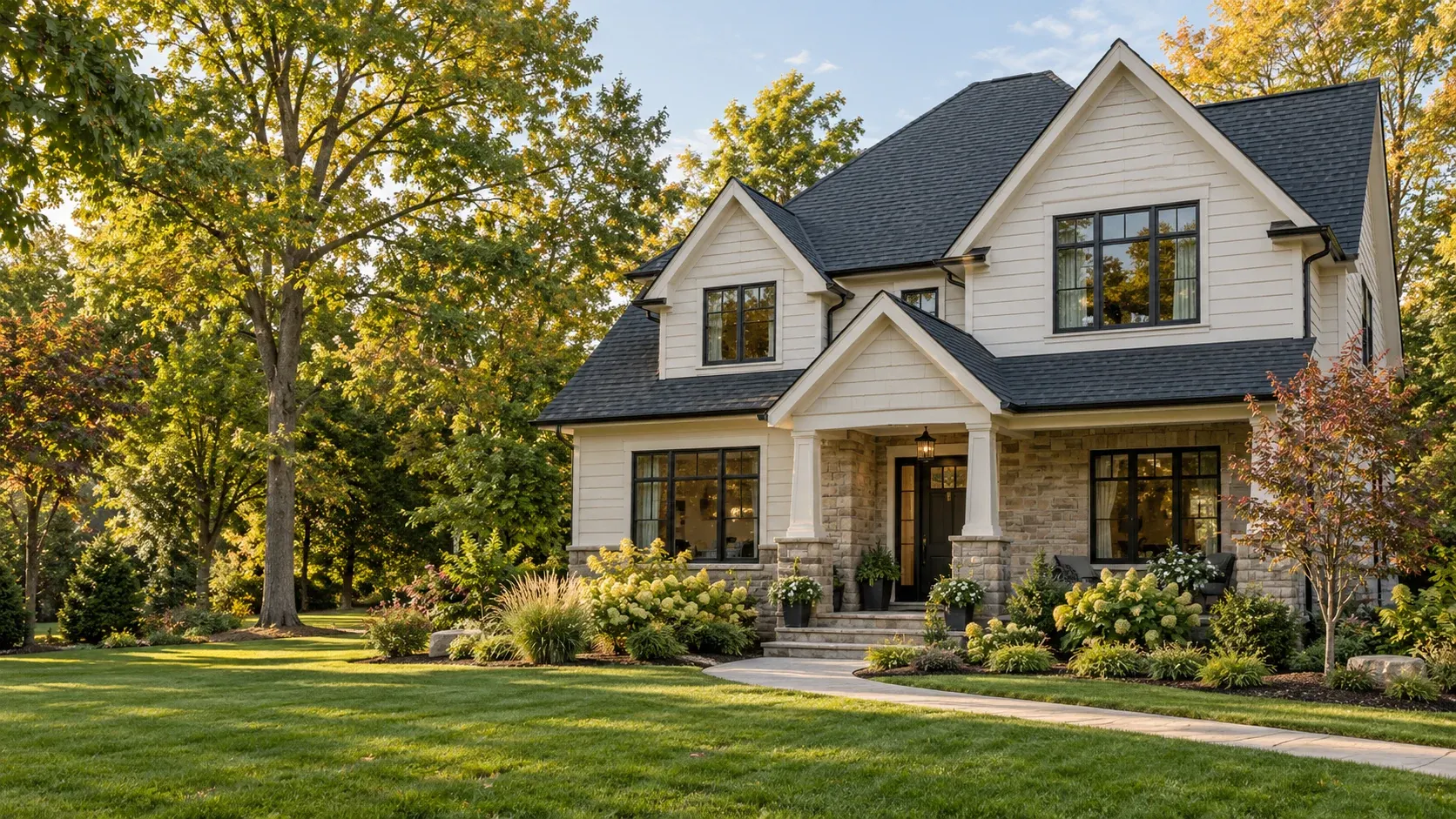 Modern two-story home with white siding, dark roof, stone foundation, and manicured front lawn surrounded by mature trees