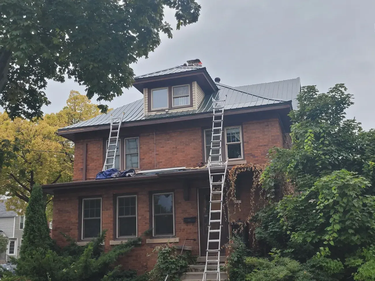 Red brick Victorian house with metal roof and extension ladders leaning against facade
