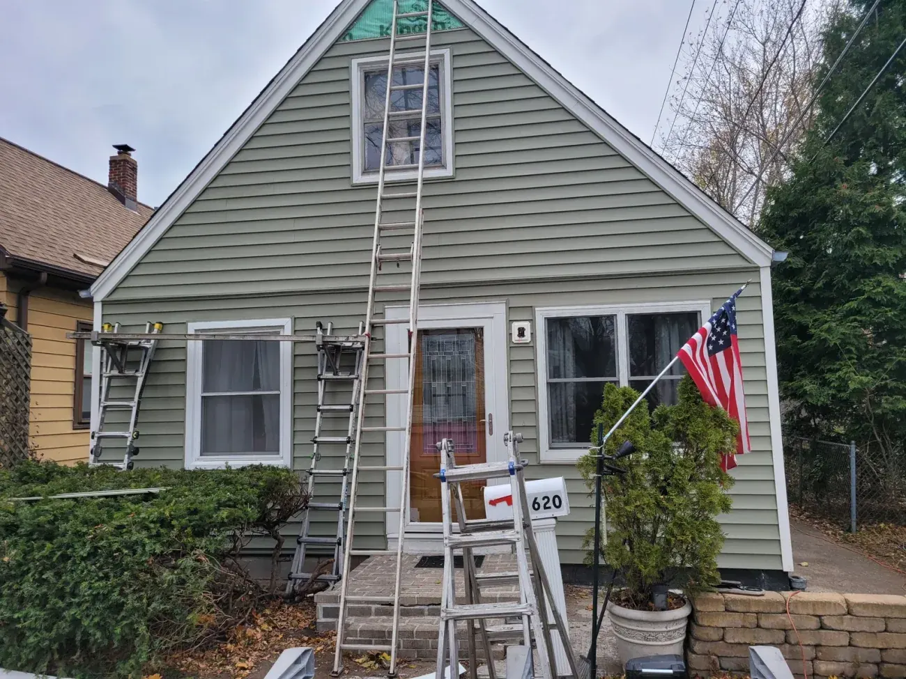 Gray house with white trim, gable roof, American flag, and ladders leaning against facade at 620