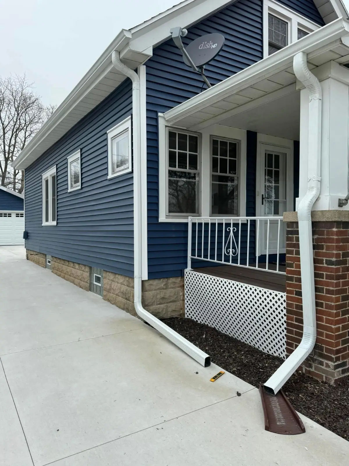 Modern blue and white house with covered porch, white railings, and brick foundation