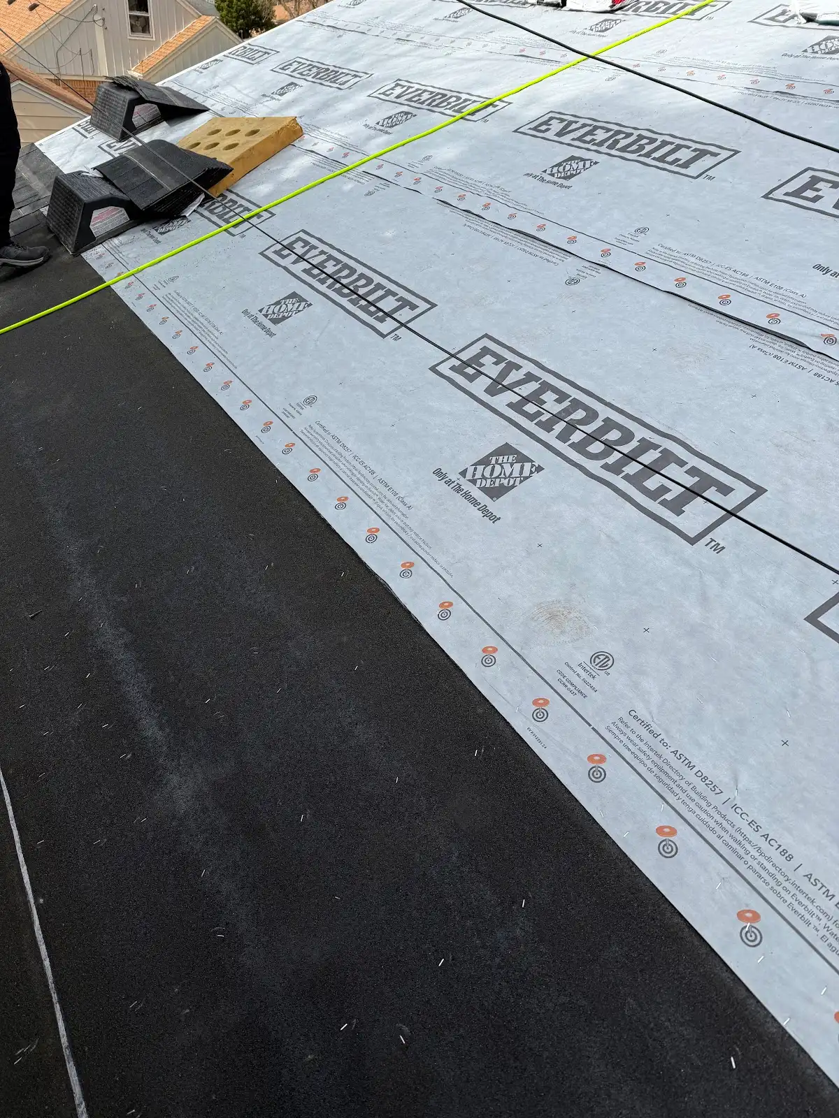 Roofing underlayment sheets laid out with yellow chalk line and installation tools on asphalt shingles