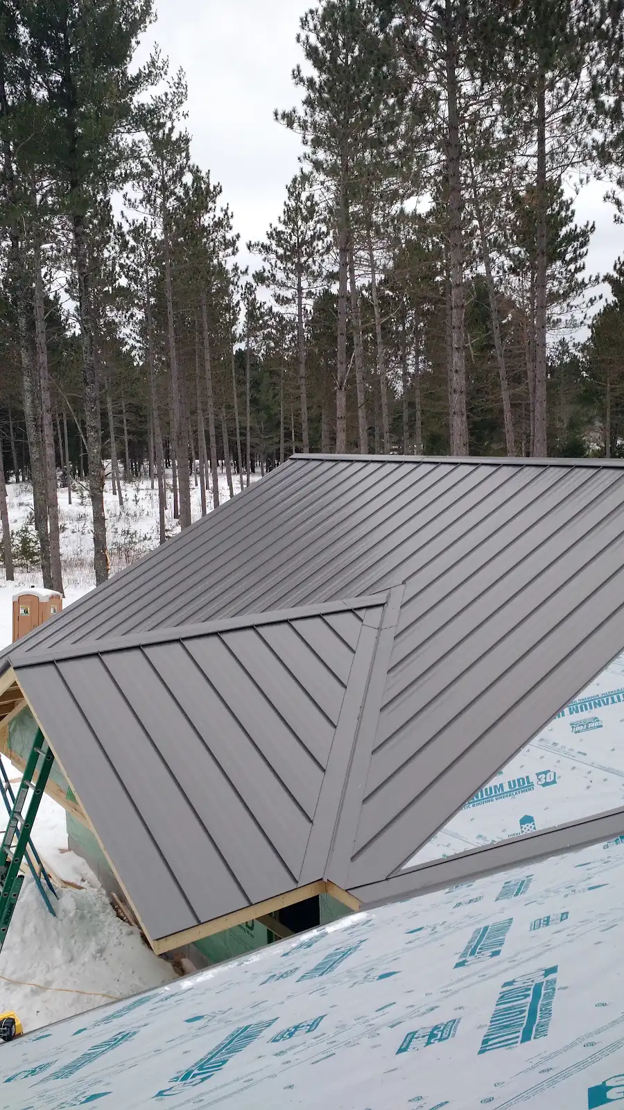 Standing seam metal roof installation on residential structure surrounded by pine forest