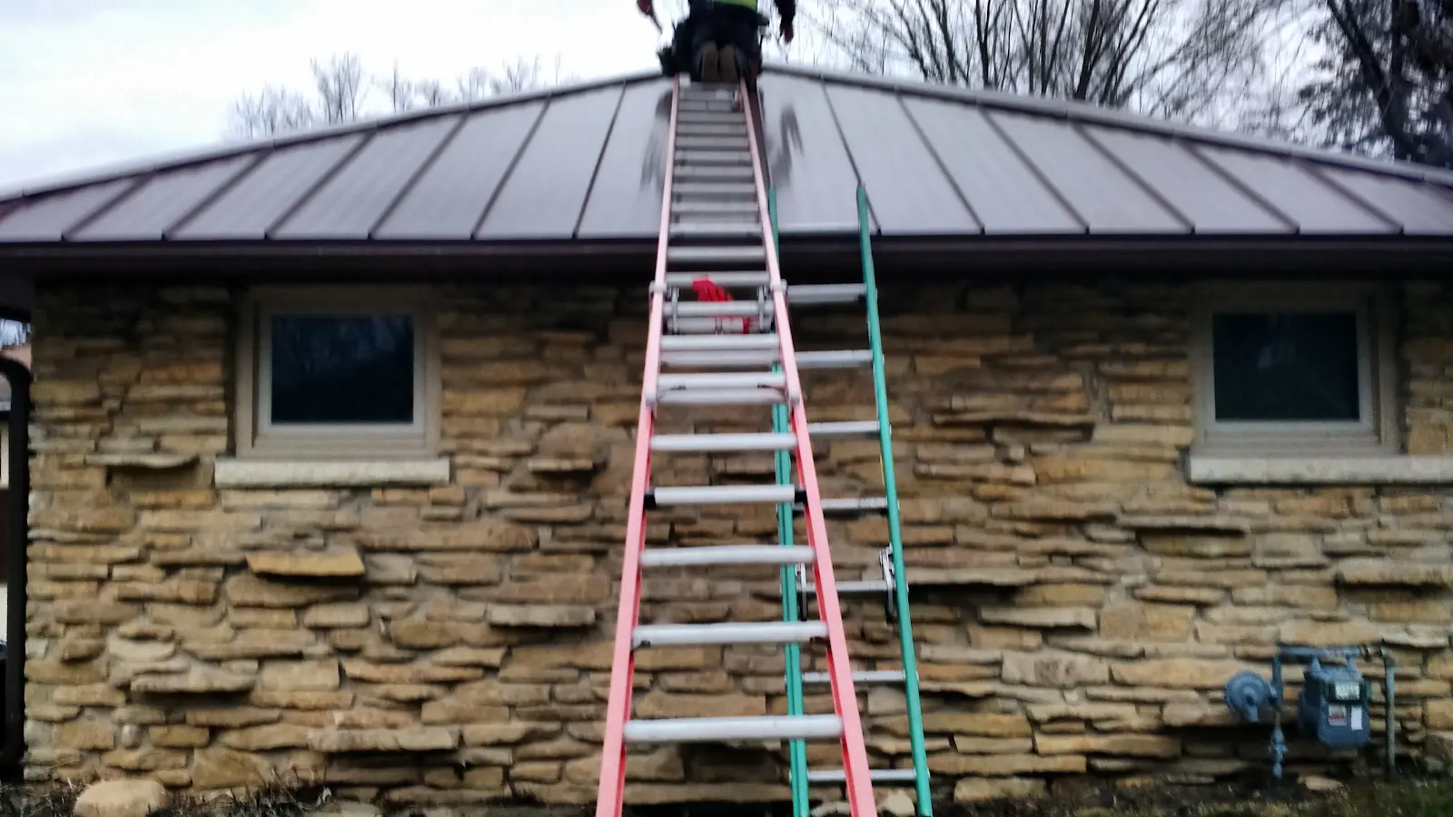 Two ladders leaning against a stone house with metal roof for roof work