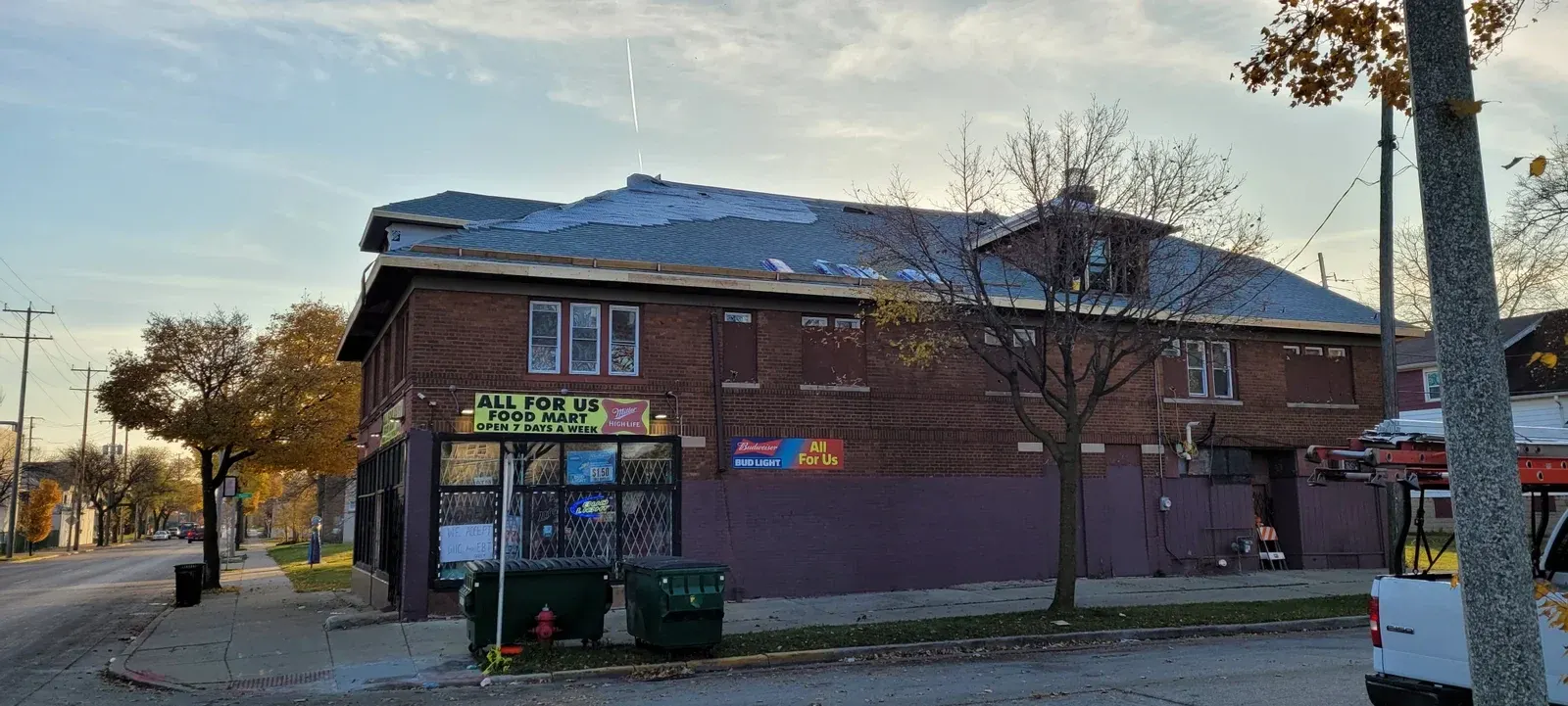 Brick building with blue roof housing All For Us Food Mart, open 7 days a week, with storefront windows and signage