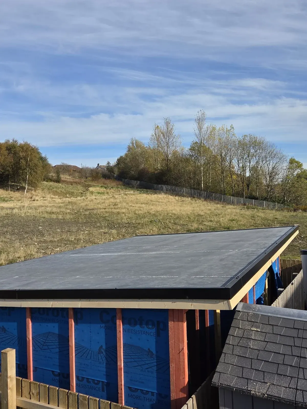 Roofing installation on hillside building with blue walls and pastoral landscape